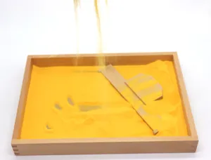 Montessori wooden sand tray detail showing scraping tool and yellow sand for early education skills.