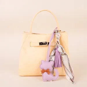 Detailed view of elegant yellow handbag featuring a cute purple cat charm and silk scarf.