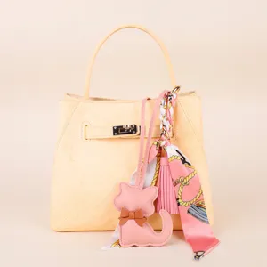 Detailed close-up shot of light yellow handbag with cute pink cat charm and silk scarf.
