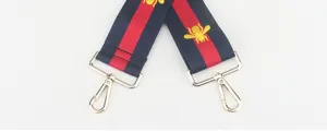 Detailopname van gestreepte vervangende tassenriem met gouden geborduurde bij en zilveren haken.