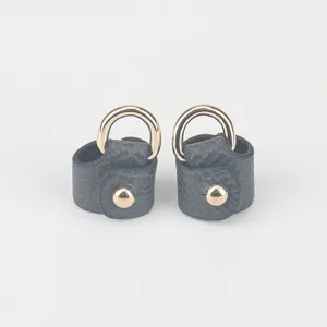 Gedetailleerd close-up van donkergrijze leren tasriem-ombouwlus met gouden ring en drukknop.