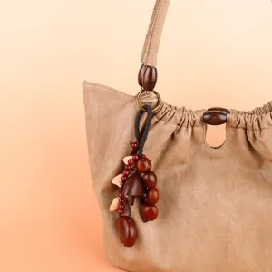 Handmade natural fruit shell pendant detail on beige leather bag, unique forest style accessory.