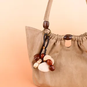 Detailed view of khaki leather handbag with natural seed pod pendant and wooden bead accents.