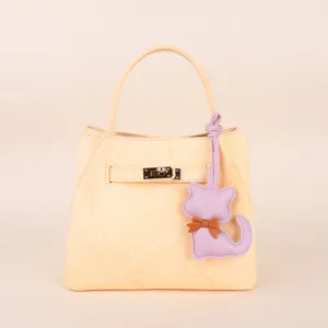 Cream leather handbag with top handle and cute purple cat keychain charm accessory.