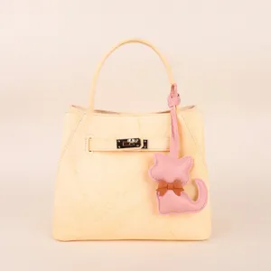 Stylish light yellow leather handbag with cute cat charm and metal lock closure.