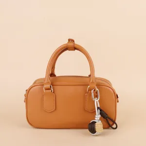 Brown leather handbag detail featuring stylish braided ball pendant and metal hardware.