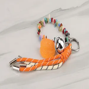 Detailed view of colorful braided keychain with gemstone beads, metal bell and orange charm.