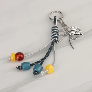 Detailed view of colorful braided keychain charm with metal bow, heart pendant and beads.