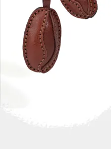 Close-up detail of brown leather coffee bean charm, fine hand-stitching texture and shape.