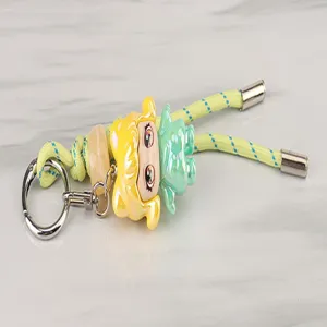 Detailed view of a cute cartoon doll pendant braided keychain with metal ring and yellow rope.