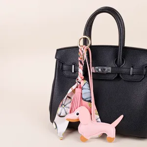 Pink leather dachshund bag charm detail, featuring braided twilly scarf and elegant tassel accessory.