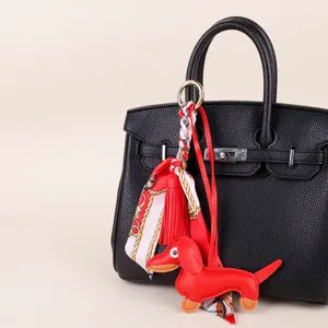 Dachshund dog bag charm detail view, red leather keychain with silk scarf and tassel decor.