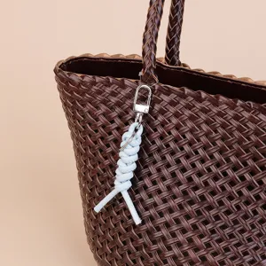 Detailed view of brown leather woven handbag featuring a chic light blue braided keychain charm.