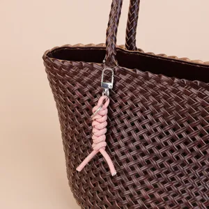 Close-up detail of a dark brown woven leather handbag paired with a cute pink keychain strap.