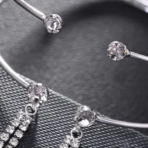 Dettaglio ravvicinato di bracciale da braccio aperto in metallo argentato con strass e nappe.