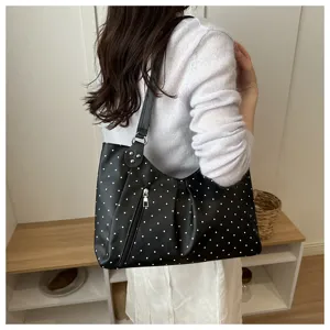 Detail shot of a black and white polka dot shoulder tote bag worn by a model in a casual indoor setting.