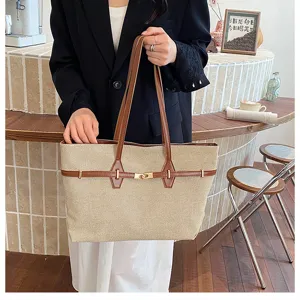 Canvas tote bag detail view showing brown leather straps and turn lock closure in cafe setting.
