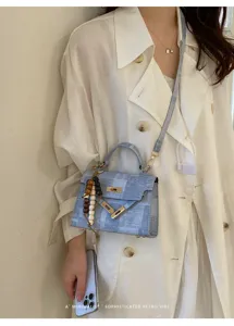 Chic sac bandoulière Kelly en jean bleu avec serrure dorée élégante et pendentif en perles.