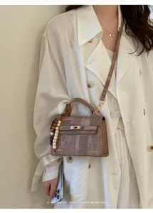 Sac à main élégant pour femme à motif rétro, fermoir métallique et charm de perles chic.