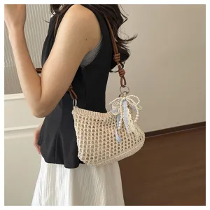 Detail view of a beige crochet crossbody bag with a blue bow and pearl strap decoration.
