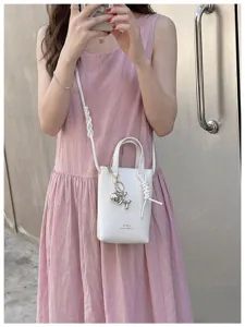 Vue rapprochée du sac bandoulière vertical blanc minimaliste avec un pendentif chien ballon.