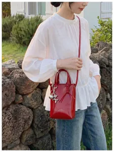 Vue détaillée du sac bandoulière seau rouge verni, design minimaliste chic avec porte-clés.