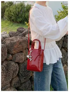 Petit sac cabas rouge vernis avec bandoulière et charm métallique, vue détaillée.