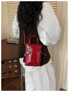 Détail de mini sac à bandoulière rouge verni avec breloque métallique et fermeture éclair.