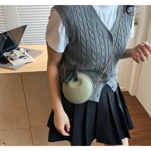 Detail view of mini apple-shaped crossbody bag with green leaf tag and metal chain strap.
