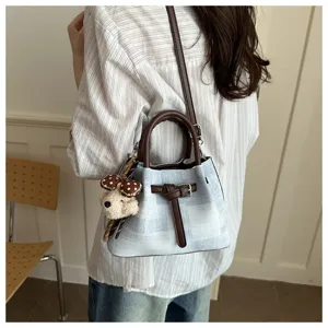Detail view of trendy casual plaid bucket bag with cute bear pendant and brown leather handle.