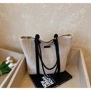 Detailopname van een geweven strooien totebag met zwarte touwvatten rustend op een boek.