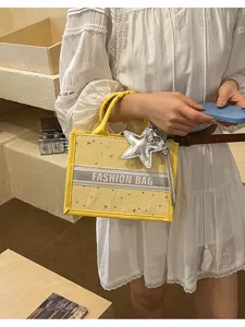 Yellow canvas tote bag detail, featuring a stylish star charm and striped front handle design.