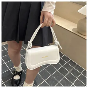 Detail shot of white underarm bag featuring knotted straps and curved flap for chic fashion.