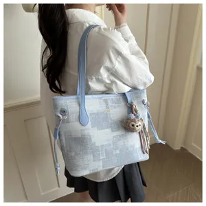 Nahaufnahme einer blauen Mustertasche aus Canvas mit Schulterriemen und Plüschanhänger.