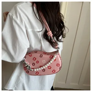 Vue rapprochée d'un sac porté épaule rose avec des imprimés lèvres et une chaîne en perles.