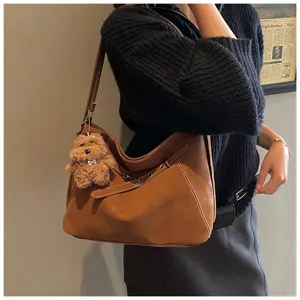 Detailansicht der braunen Retro Leder Umhängetasche mit Kontrastnähten und süßem Bärenanhänger.
