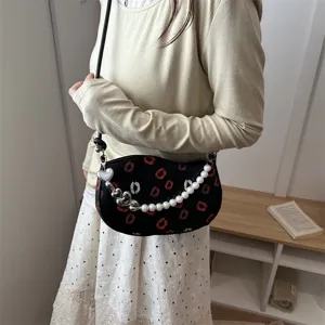 Sac bandoulière croissant noir chic avec imprimé lèvres rouges et chaîne de perles.