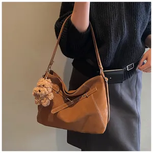 Detailansicht der braunen Retro-Umhängetasche mit plüschigem Bärenanhänger und Metallschnallen.