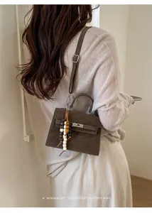 Detailed view of a chic brown retro shoulder bag with wooden bead charm on a model.