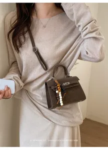 Detailed view of stylish brown leather crossbody bag with wooden bead charm worn by model.