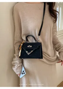 Black suede Kelly handbag detail shot featuring silver hardware and a chic wooden bead charm.