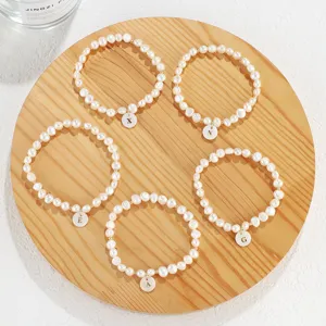 Freshwater pearl initial pendant bracelet set featuring alphabet charms on a round wooden tray.