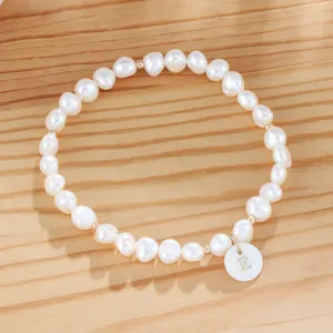 Detail view of a freshwater pearl bracelet featuring a custom initial letter pendant on wood.