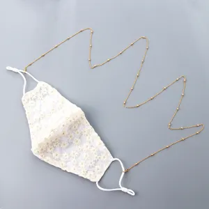 Delicada mascarilla de encaje floral con elegante cadena dorada de cuentas para diario.