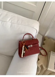 Détail du sac Kelly en cuir rouge vin, avec fermoir tourniquet en métal et breloque en perles.