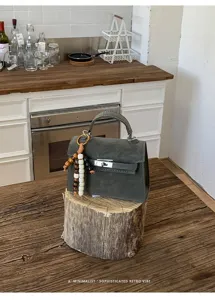 Détail de sac à main Kelly en suède vert foncé, avec fermoir en métal et support en bois.