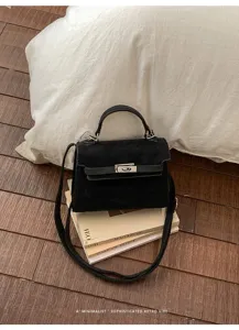 Gros plan détaillé du sac à main Kelly en daim noir sur des livres, ambiance rétro et épurée.