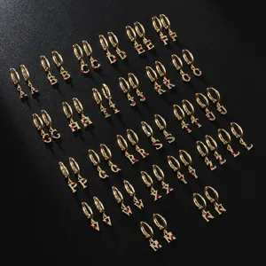 Gold alphabet letter hoop earrings with red crystal pendant, elegant jewelry detail shot.