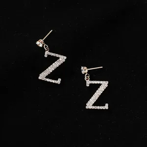 Dettaglio di orecchini con lettera Z in strass scintillanti, orecchini a lobo cristallo dorato.