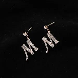 Primo piano dettagliato di orecchini con lettera M pavé di strass lucidi con design a perno dorato.